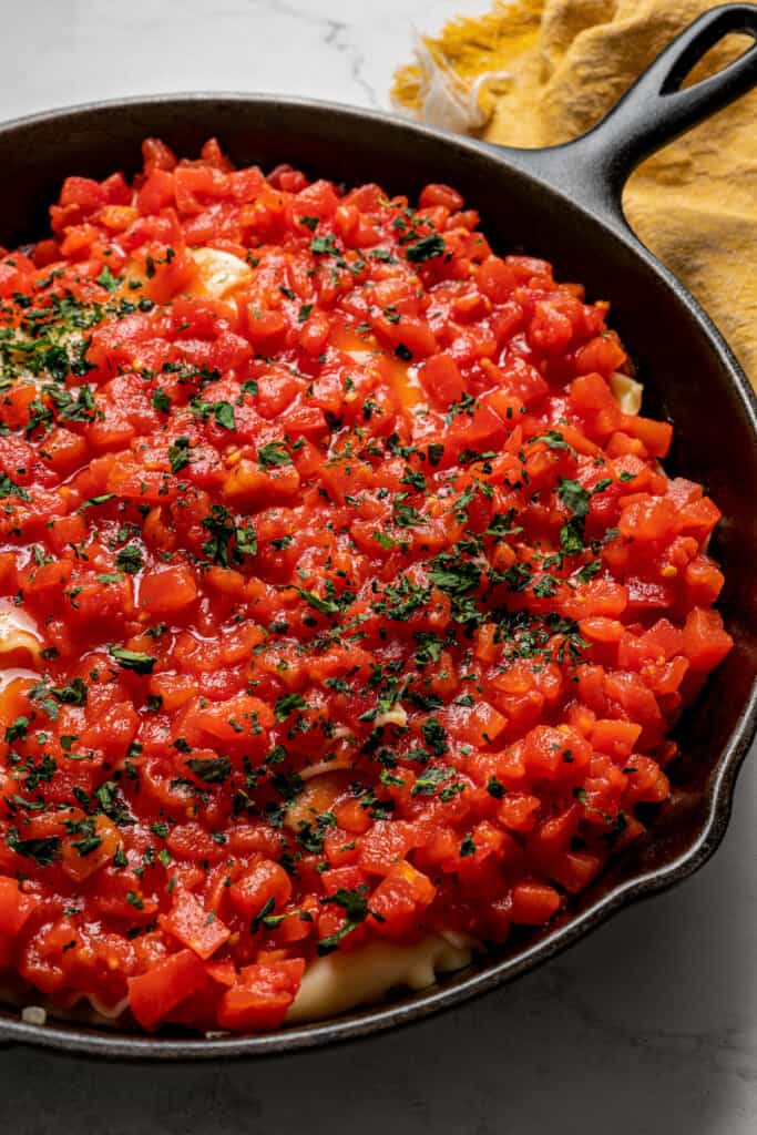 Close up of tomatoes and basil on top of lasagna in a skillet