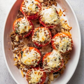 Overhead view of quinoa stuffed tomatoes topped with melted cheese in a white ceramic baking dish.