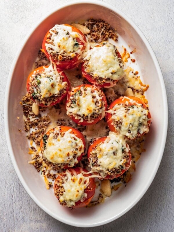 Overhead view of quinoa stuffed tomatoes topped with melted cheese in a white ceramic baking dish.