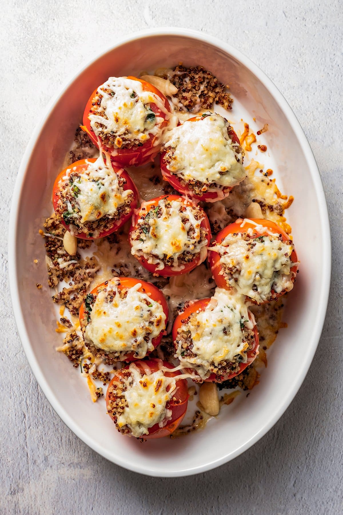 Overhead view of quinoa stuffed tomatoes topped with melted cheese in a white ceramic baking dish.