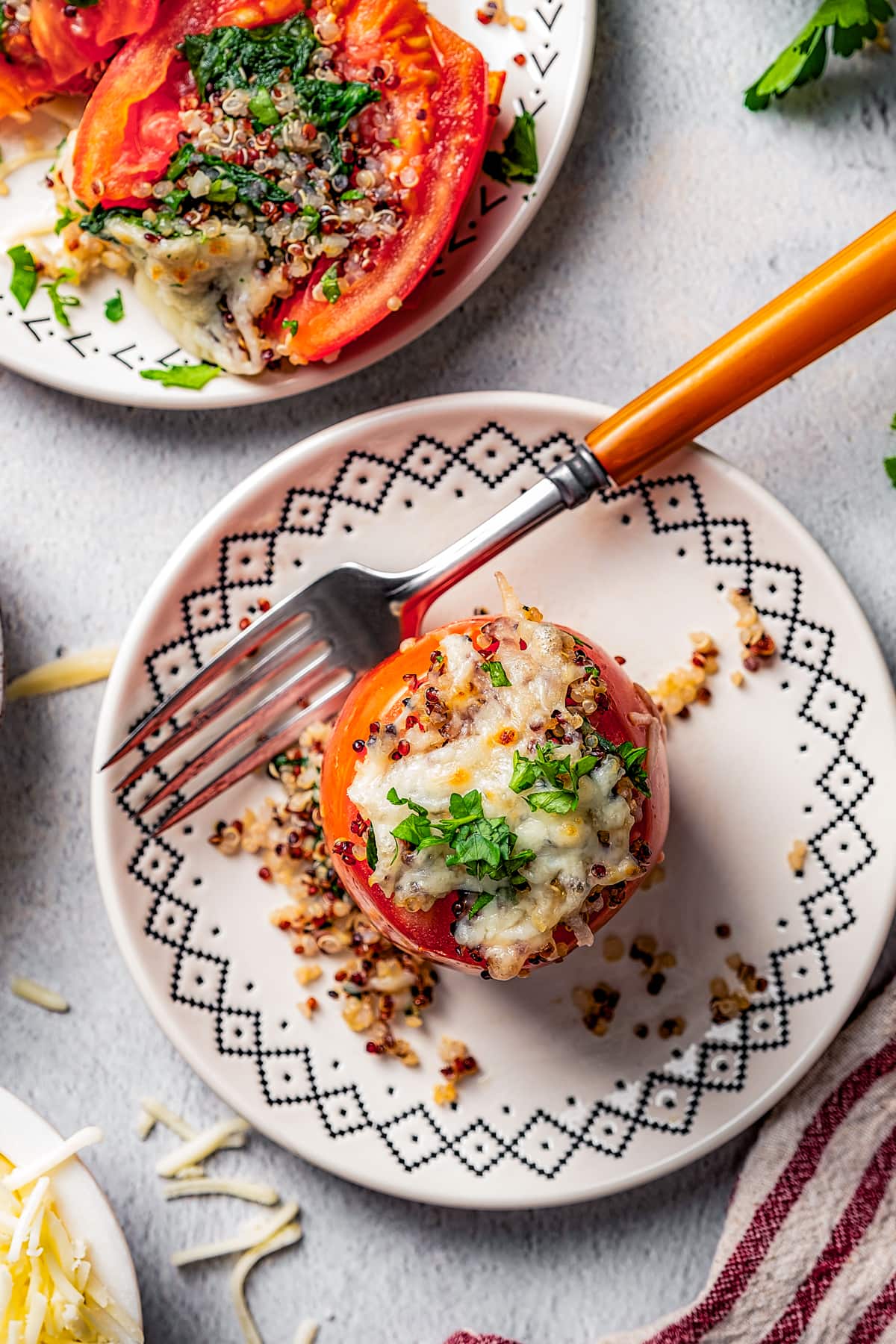 Overhead view of two quinoa stuffed tomatoes served on plates, with one stuffed tomato cut in half.