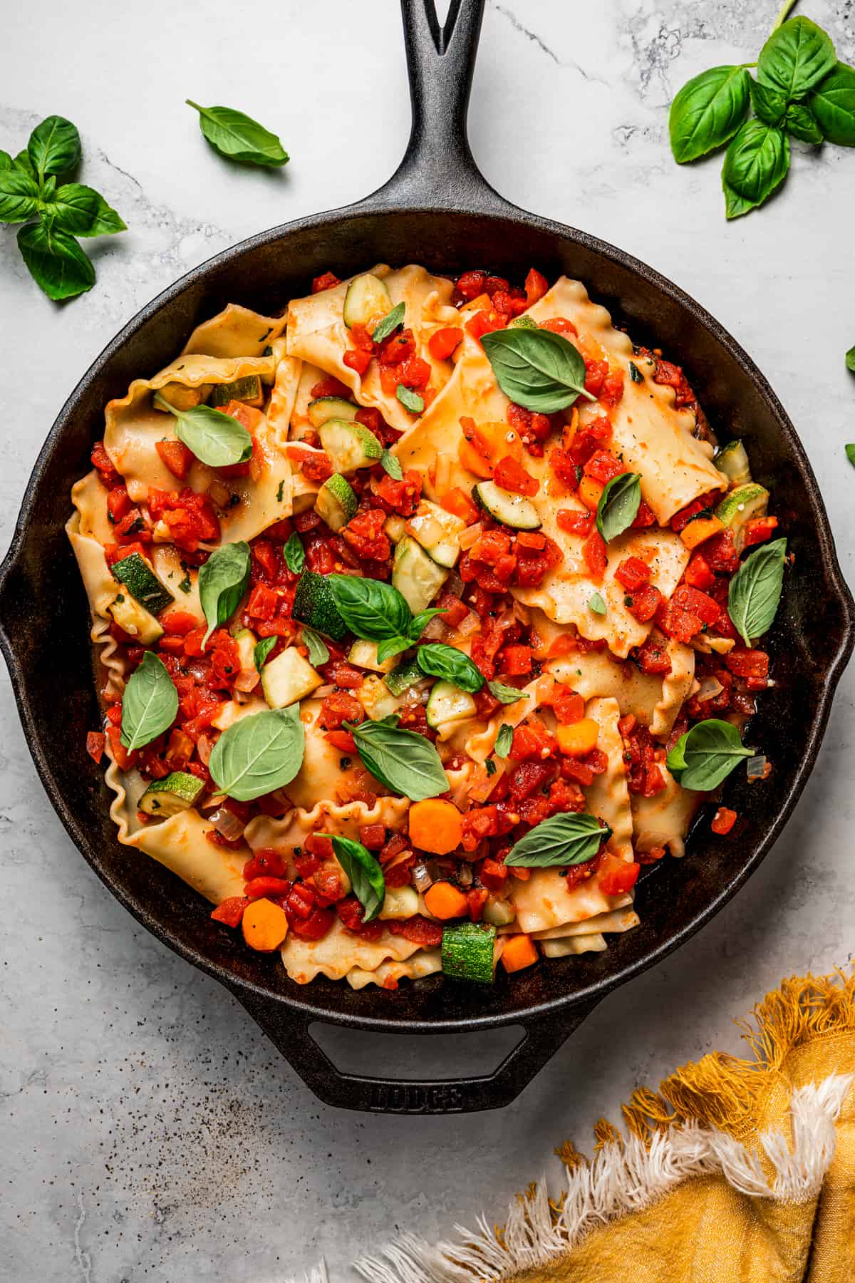 Overhead view of a skillet full of lasagna, topped with basil and diced tomatoes.