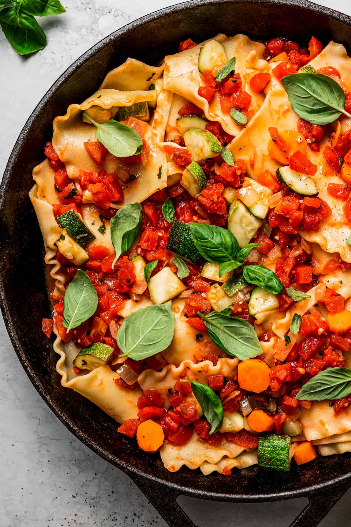 Overhead view of a skillet full of lasagna, topped with basil and diced tomatoes.