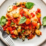 Overhead view of a plate of lasagna topped with fresh basil, and a fork placed on the dinner plate.