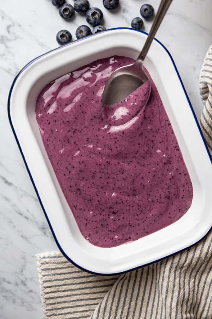 Blueberry nice cream mixture poured into a loaf pan with a spoon.