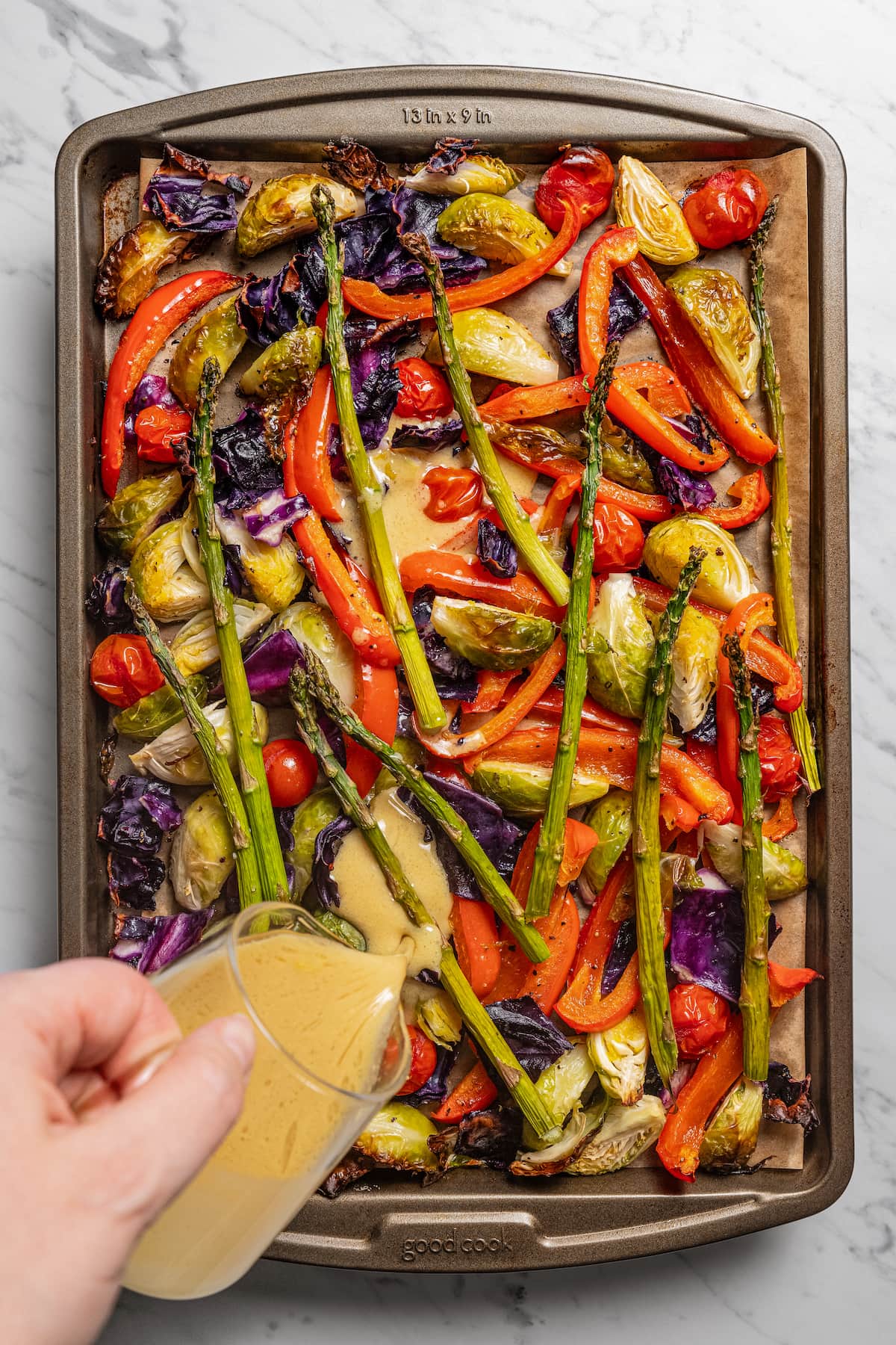 Pouring the dressing over the veggies in the baking sheet.