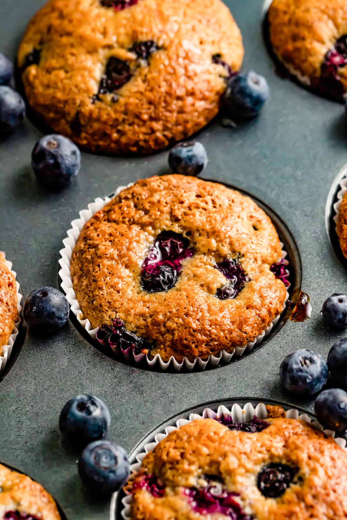 Blueberry lemon muffins baked in a muffin pan with fresh blueberries scattered around.