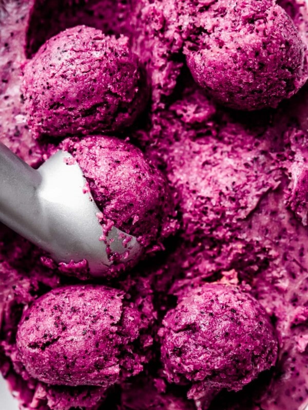 Close up of an ice cream scoop portioning balls of vegan blueberry ice cream from a loaf pan.