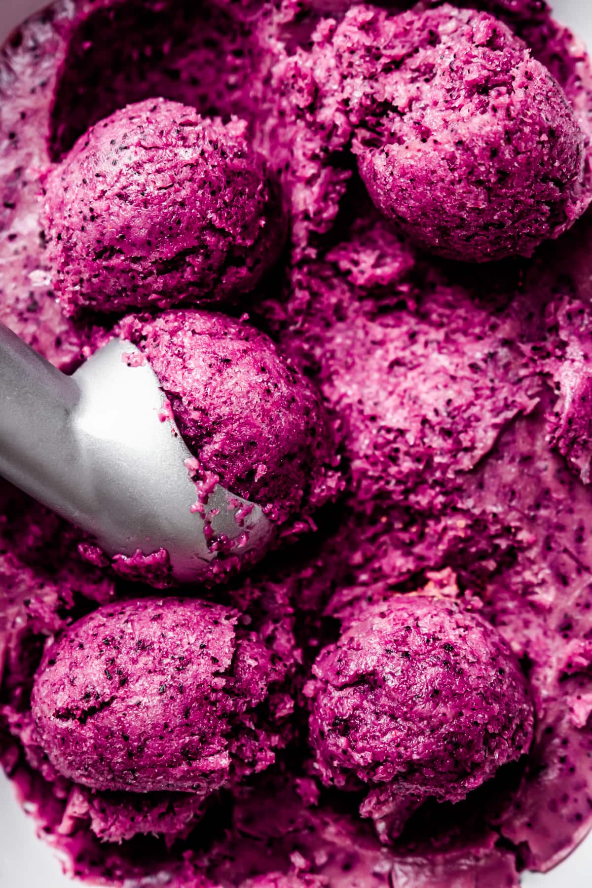 Close up of an ice cream scoop portioning balls of vegan blueberry ice cream from a loaf pan.