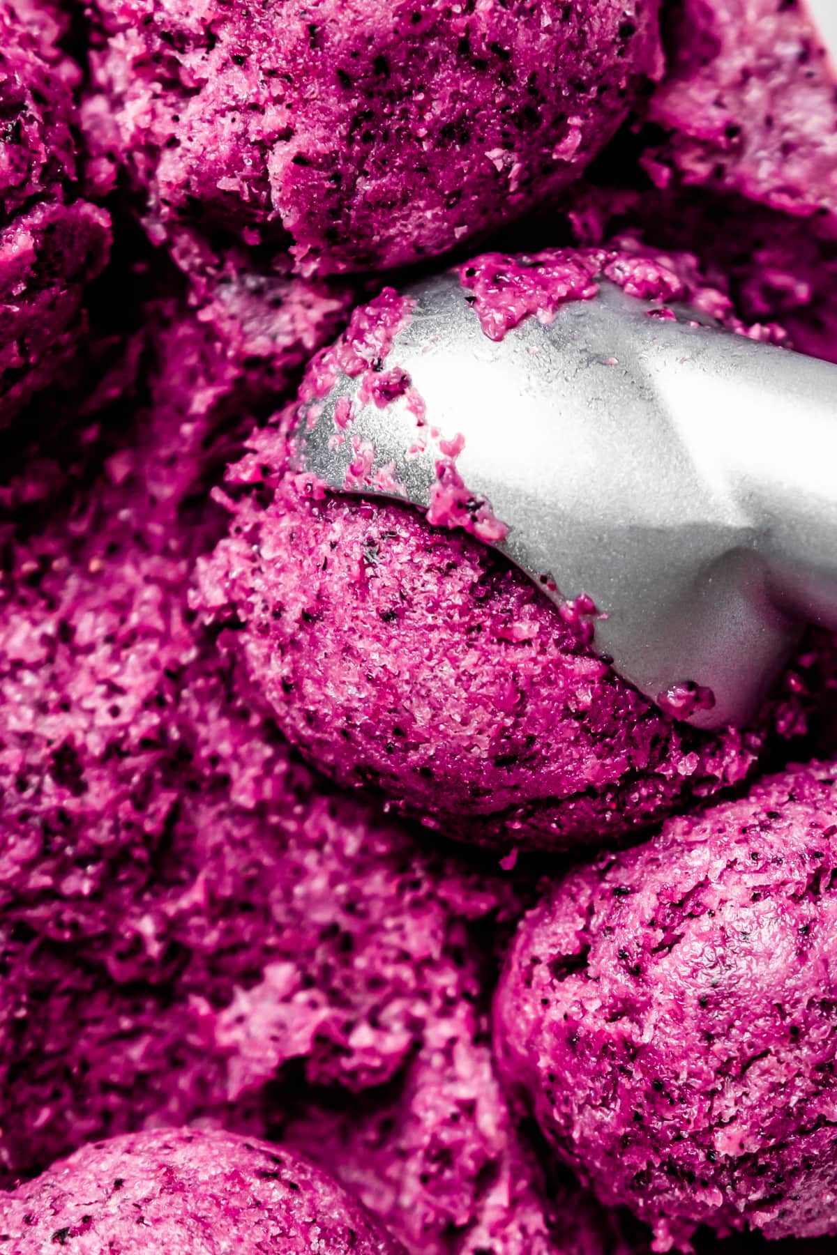 Close up of an ice cream scoop portioning balls of vegan blueberry ice cream from a loaf pan.