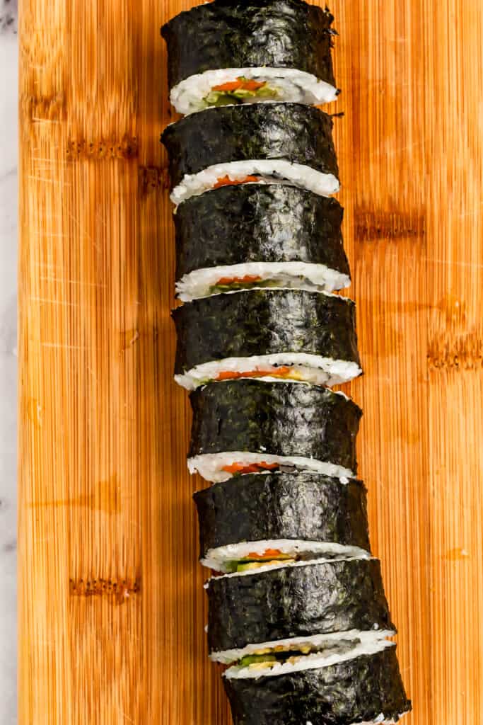 A maki roll on a wooden board sliced into pieces.