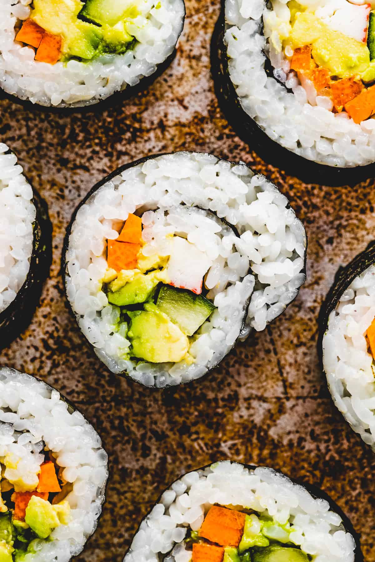 Overhead shot of several maki roll slices arranged on a brown colored backdrop.