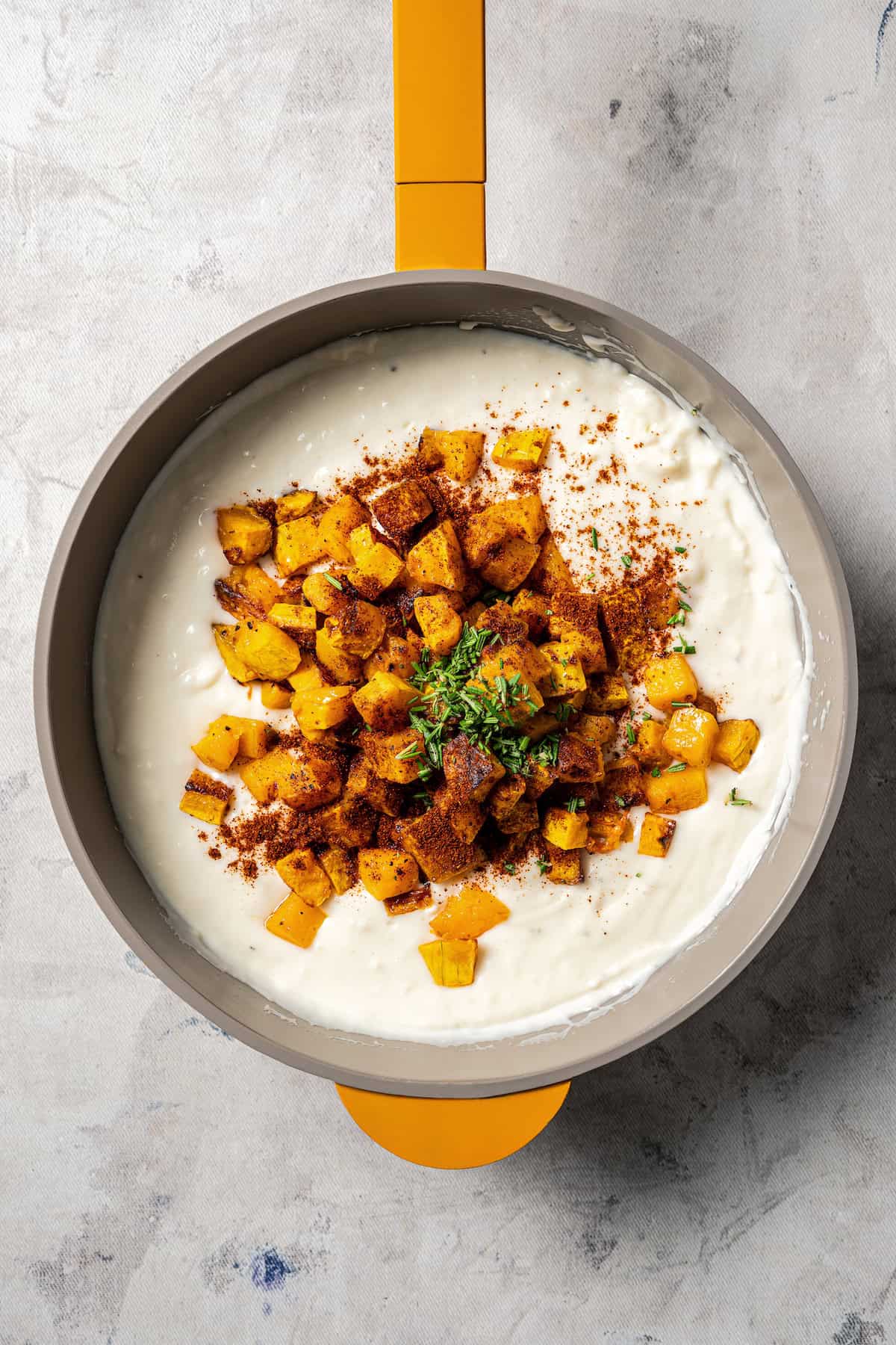 Roasted butternut squash cubes added to creamy bechamel sauce in a saucepan.