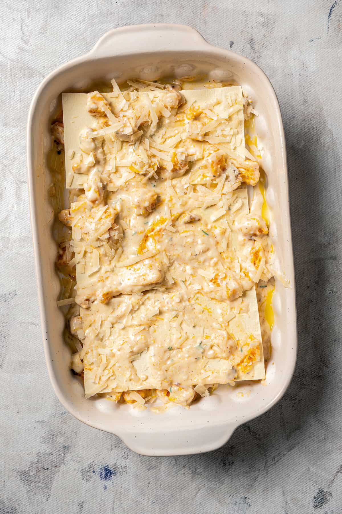 Partially assembled butternut squash lasagna in a ceramic casserole dish.