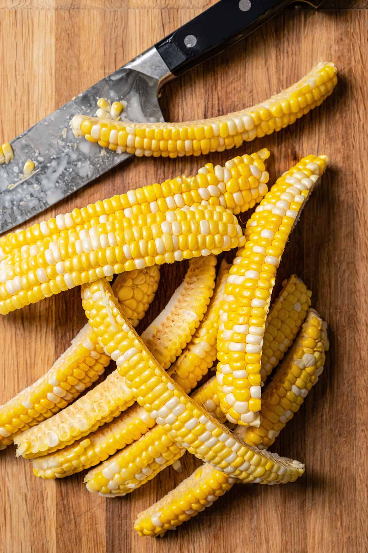 Corn on the cob cut into ribs on a wooden cutting board, next to a knife.