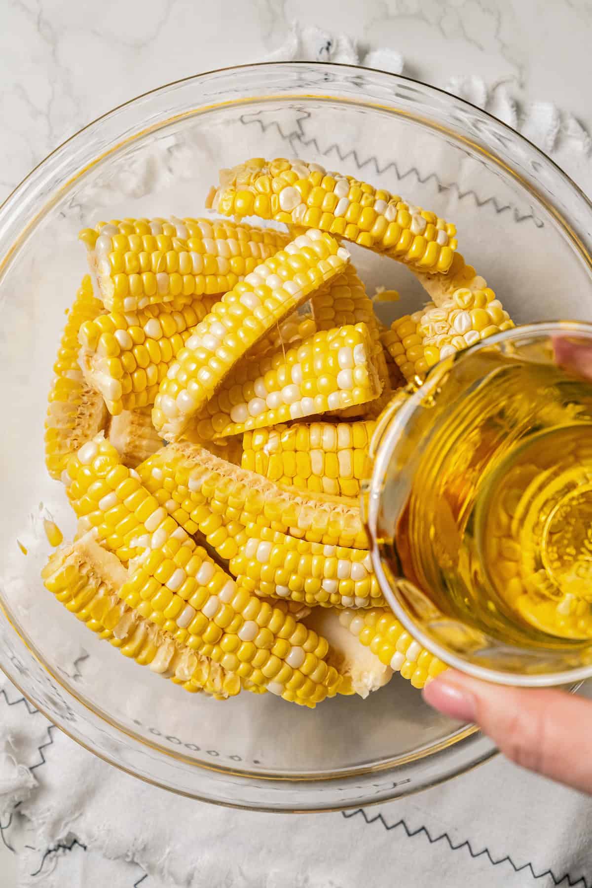 Oil being poured over corn ribs in a glass bowl.