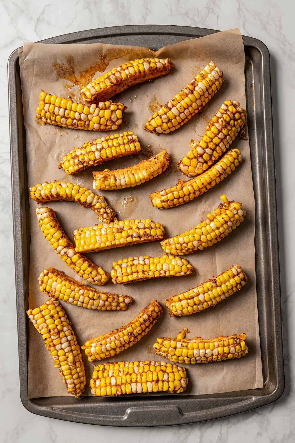 Seasoned corn ribs arranged on a lined baking sheet.