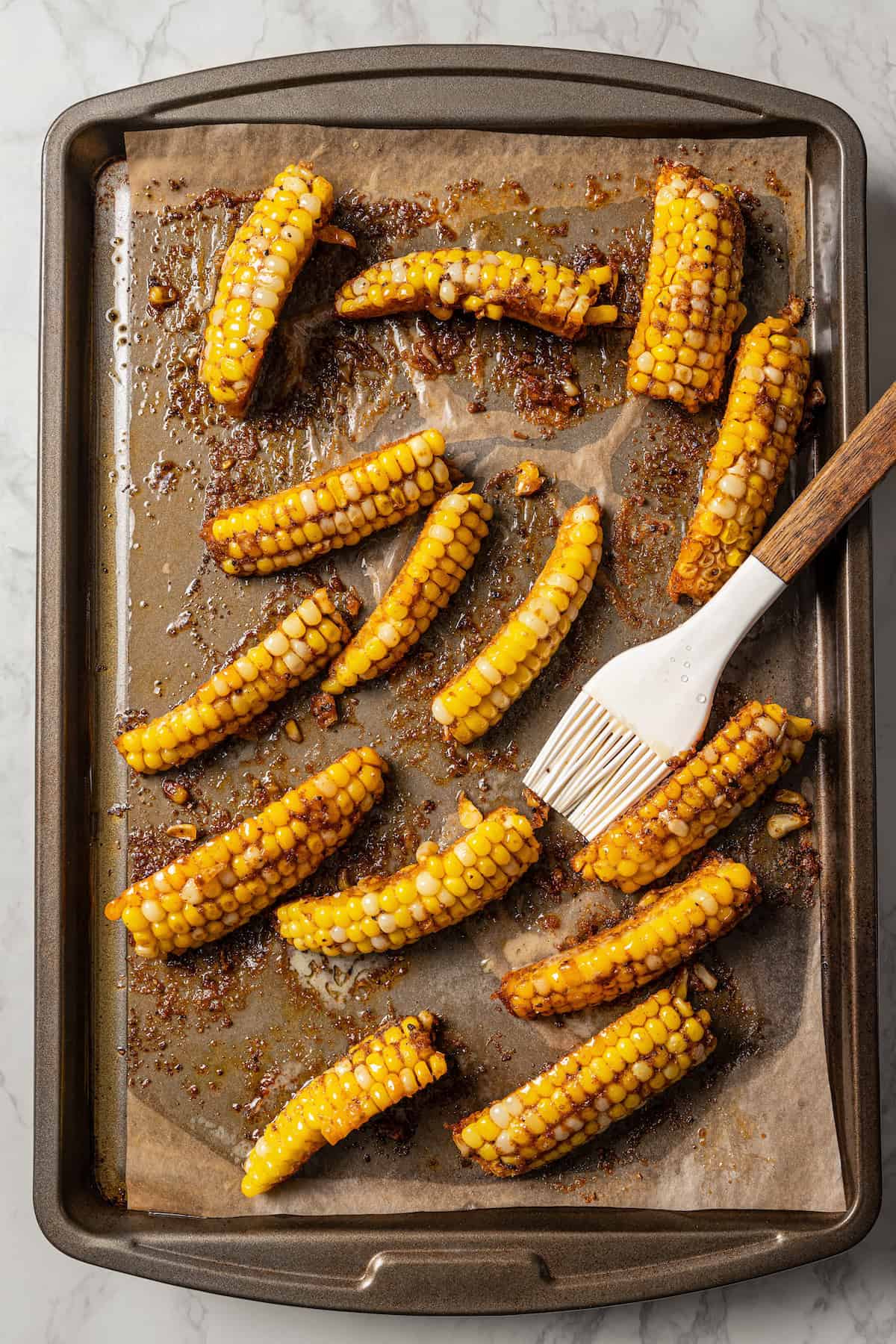 Baked corn ribs on a lined baking sheet with a basting brush.