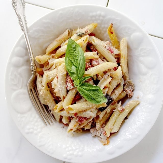 Overhead view of a serving Baked Eggplant Penne Pasta in a bowl topped with fresh basil