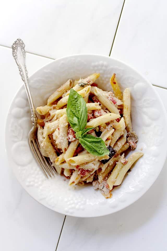 A white bowl filled with penne pasta, tomatoes, cheese and eggplant