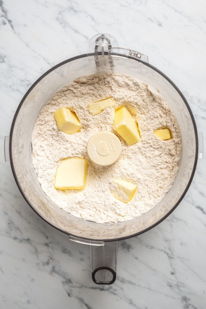 Cubed butter added to dry pizza dough ingredients in a food processor.