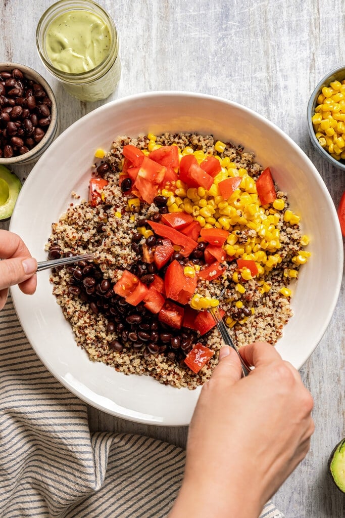 Two hands using spoons to toss quinoa Southwestern salad ingredients together in a bowl.