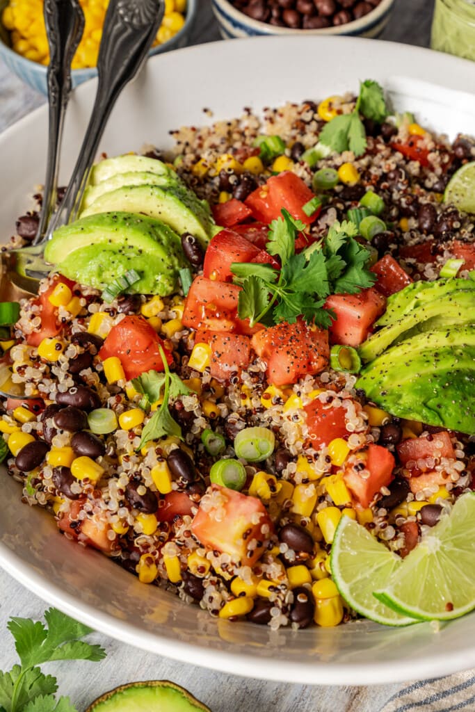 Close up view of quinoa Southwestern salad garnished with sliced avocado and lime wedges in a bowl.