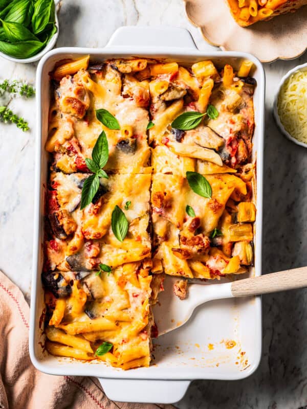 Overhead view of eggplant pasta cut into servings in a ceramic casserole dish, with a spatula resting in an open space.