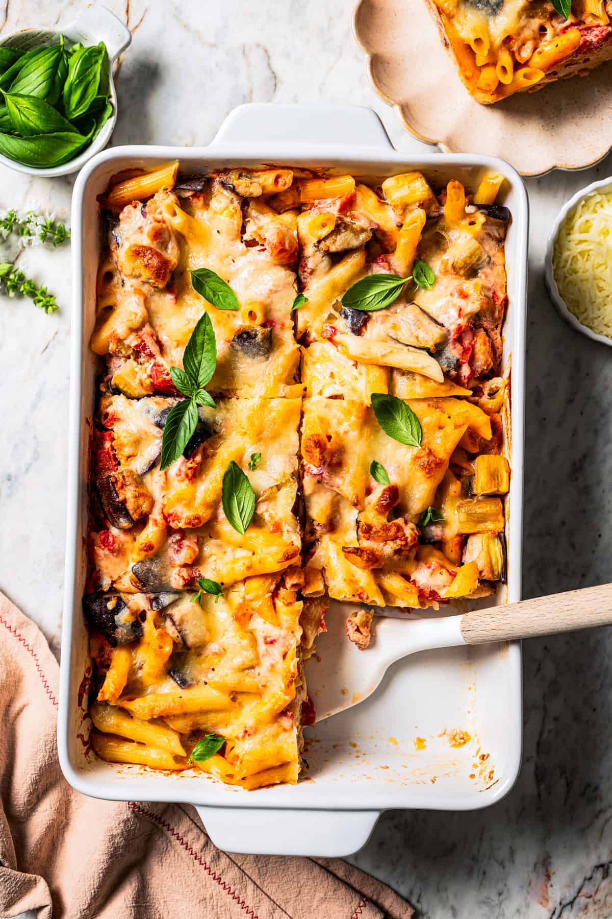 Overhead view of eggplant pasta cut into servings in a ceramic casserole dish, with a spatula resting in an open space.