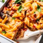 Baked eggplant penne pasta cut into servings in a ceramic casserole dish, with a spatula resting in an open space.