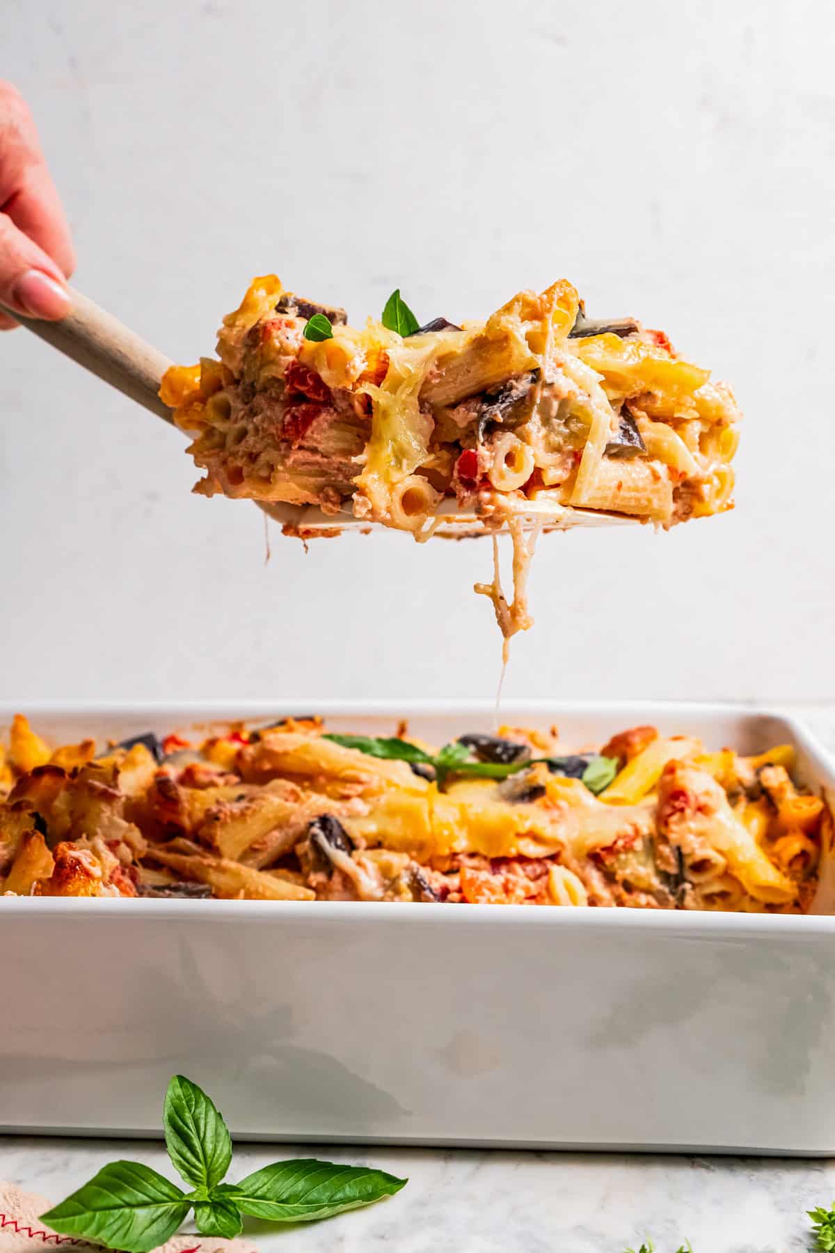 Side view of a serving of eggplant pasta being lifted above the rest of the pasta bake in a casserole dish.