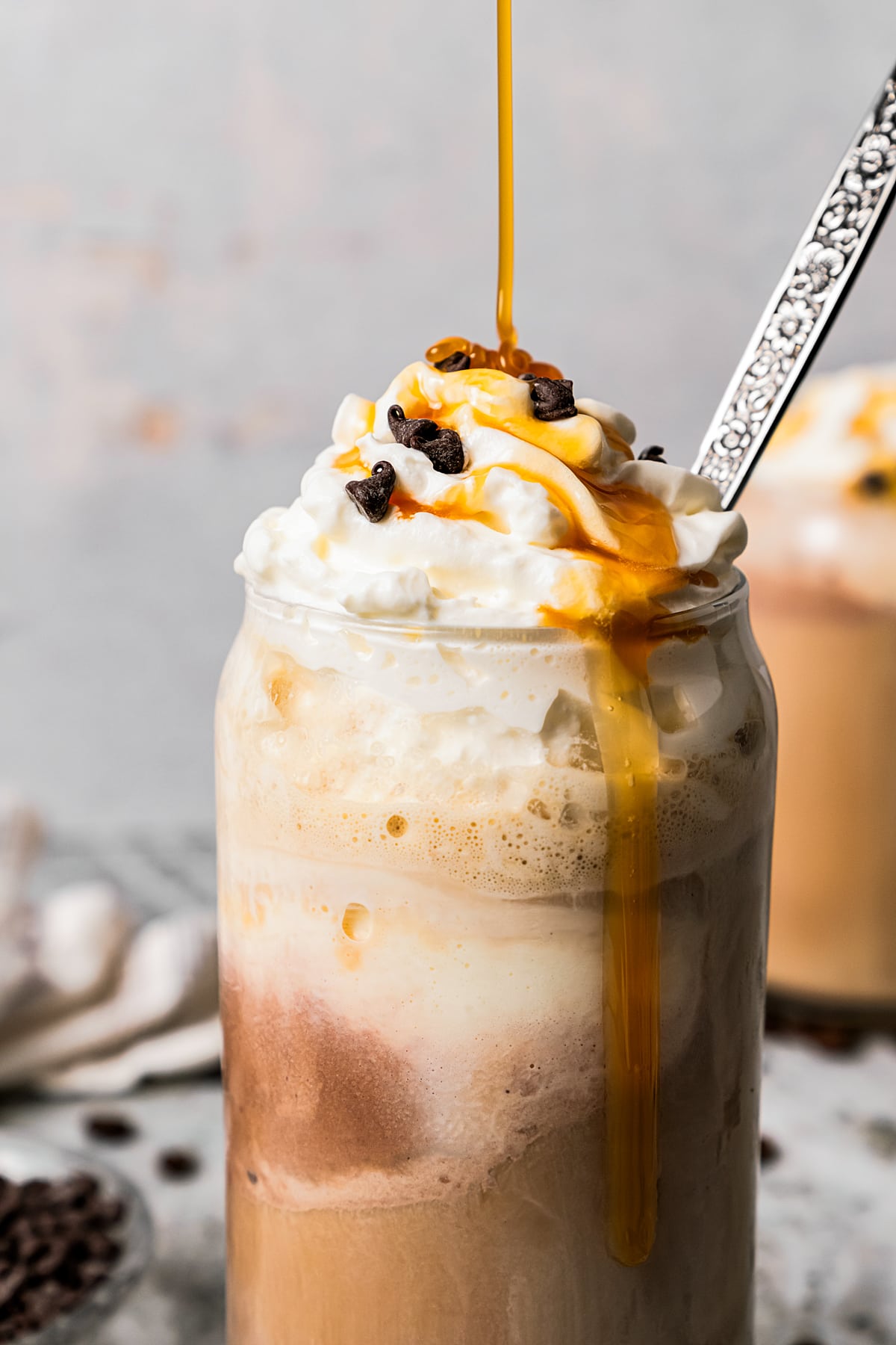 Close-up image of an ice coffee in a glass mug and topped with whipped cream, chocolate chips, and a caramel drizzle.