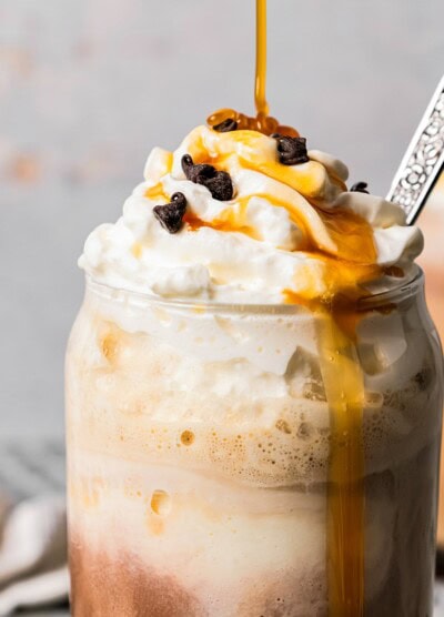 Close-up image of an ice coffee in a glass mug and topped with whipped cream, chocolate chips, and a caramel drizzle.