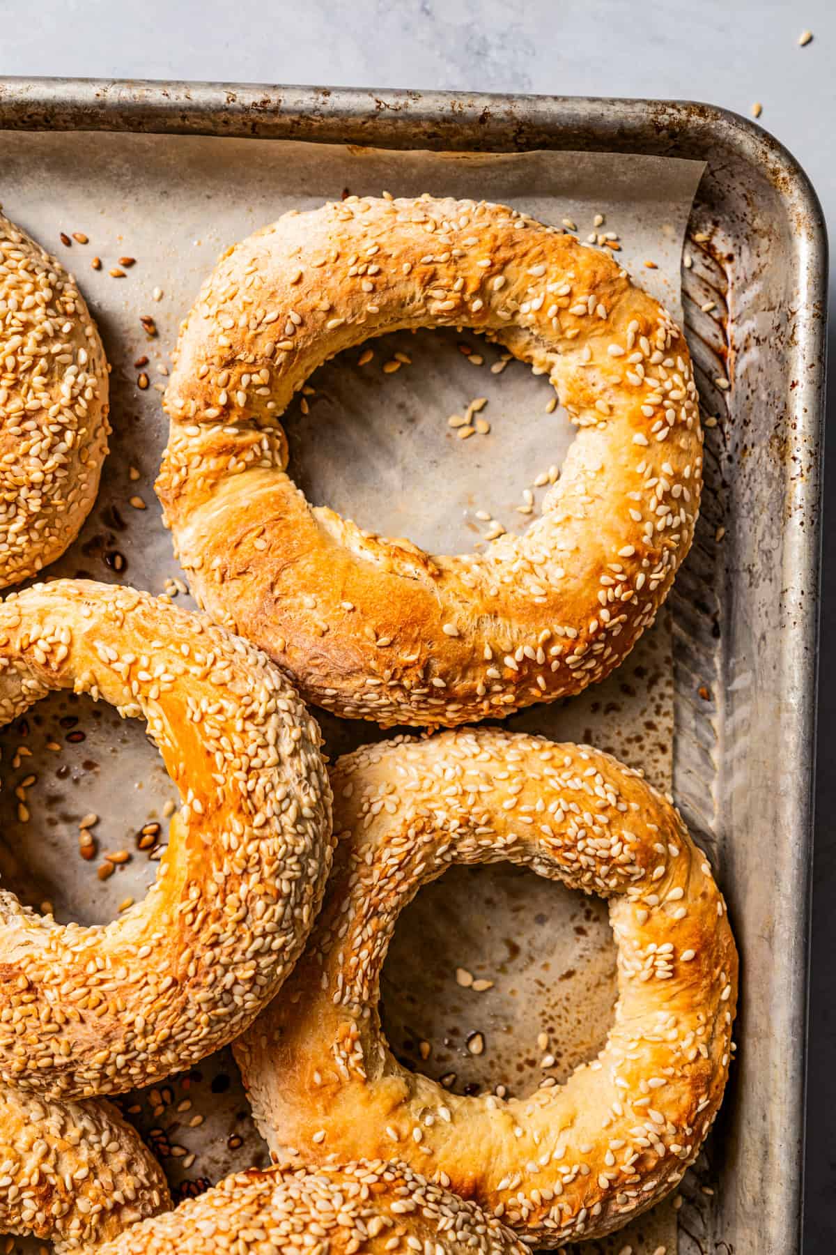 Close-up of baked sesame bagels (Gevrek) on a lined baking sheet.