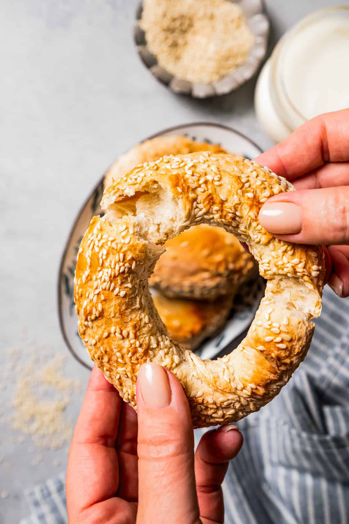 A pair of hands breaking up a sesame bagel.