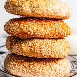 Side view of four sesame bagels stacked on a plate.