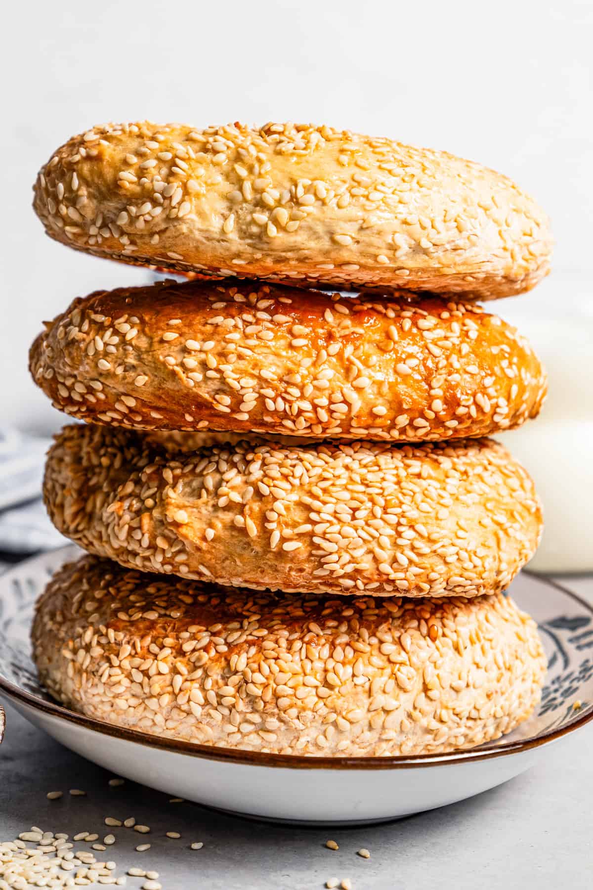 Side view of four sesame bagels stacked on a plate.