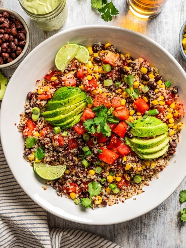 Overhead image of Quinoa Southwestern Salad in a salad bowl topped with sliced avocados and slices of lime.