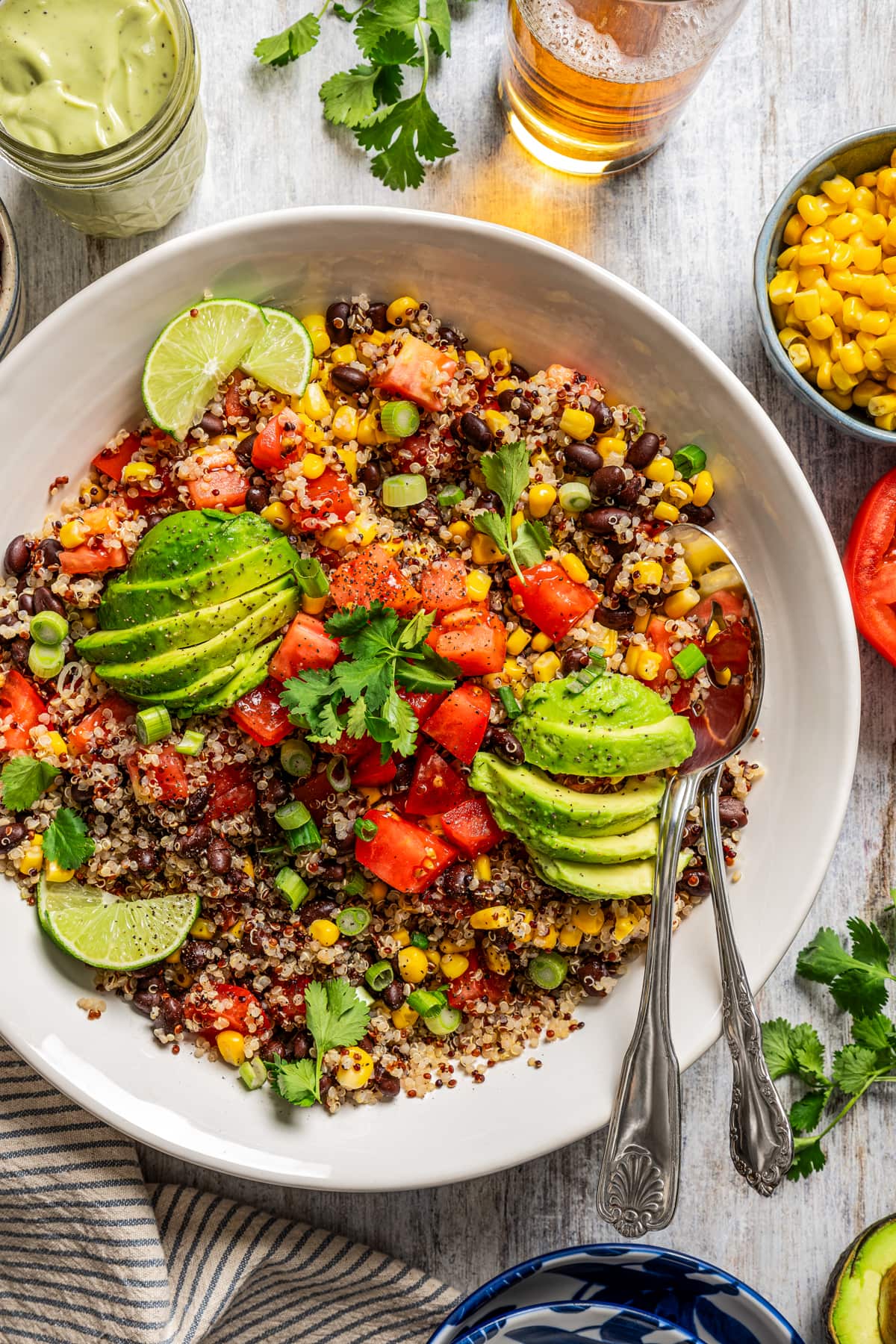 Aerial view image of a large quinoa salad in a salad bowl tossed with black beans, corn, tomatoes, and slices of avocado.