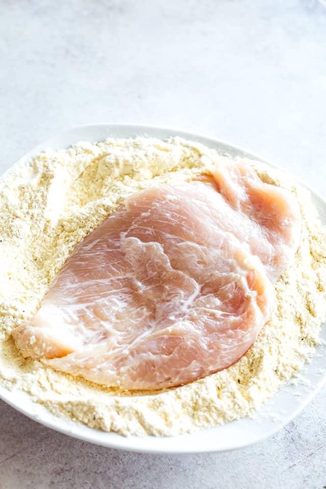 Dusting chicken breasts with flour and parmesan cheese.