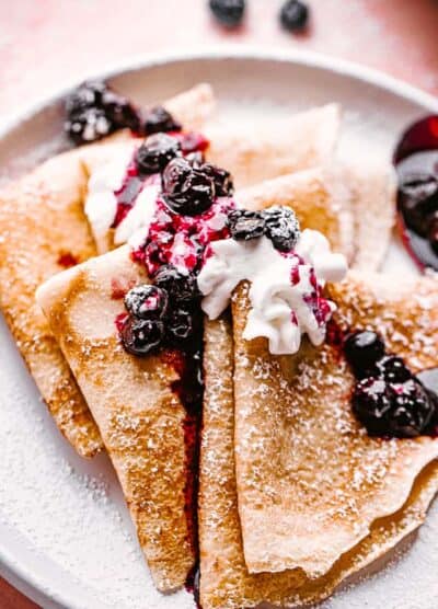 folded crepes topped with whipped cream and blueberries