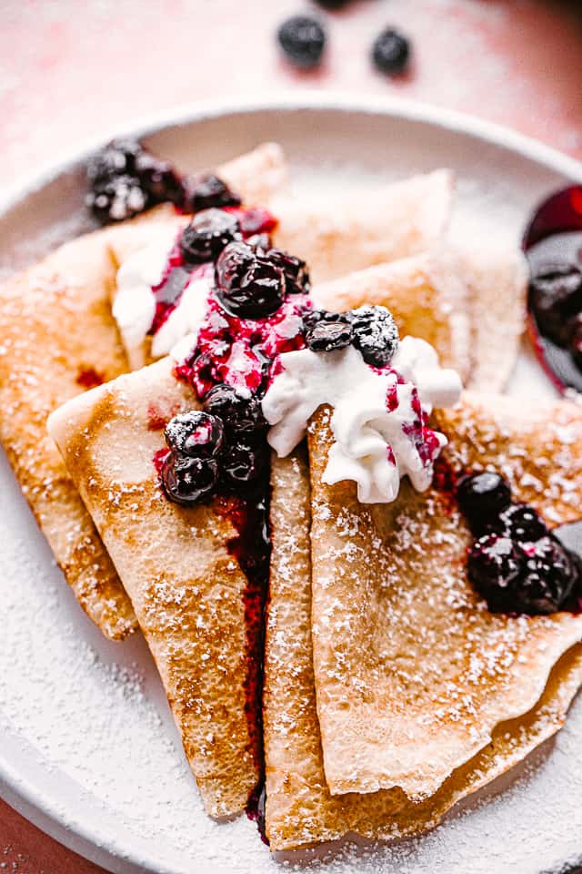 folded crepes topped with whipped cream and blueberries