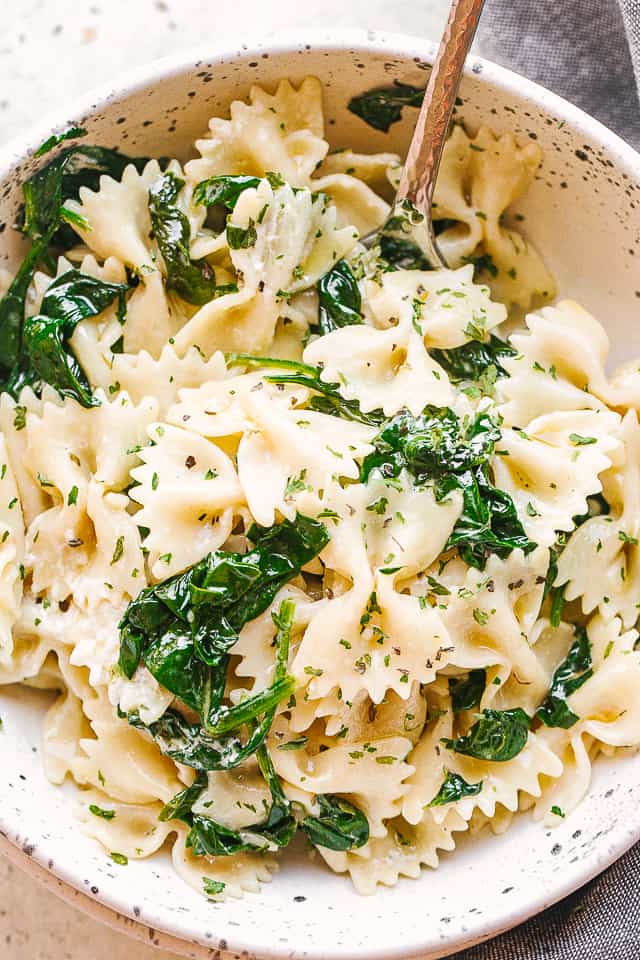 Bow tie pasta tossed with spinach and served in a bowl.