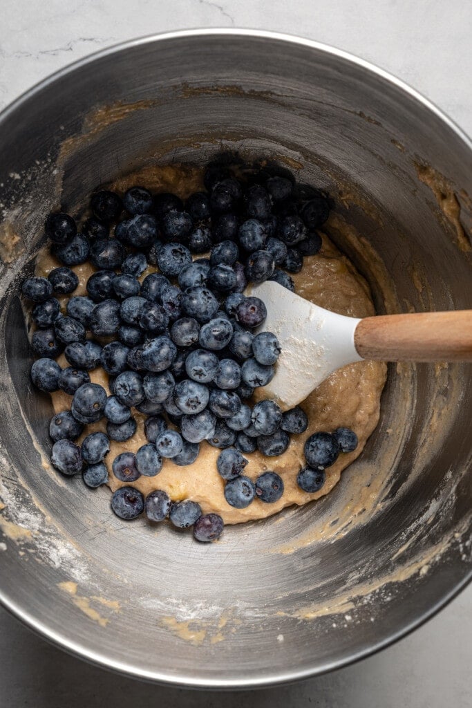 Blueberries added to banana bread batter in a metal bowl.