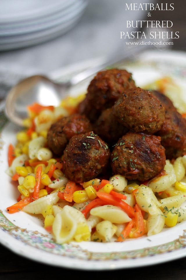 A white decorative plate filled with pasta, corn and carrots and topped with meatballs