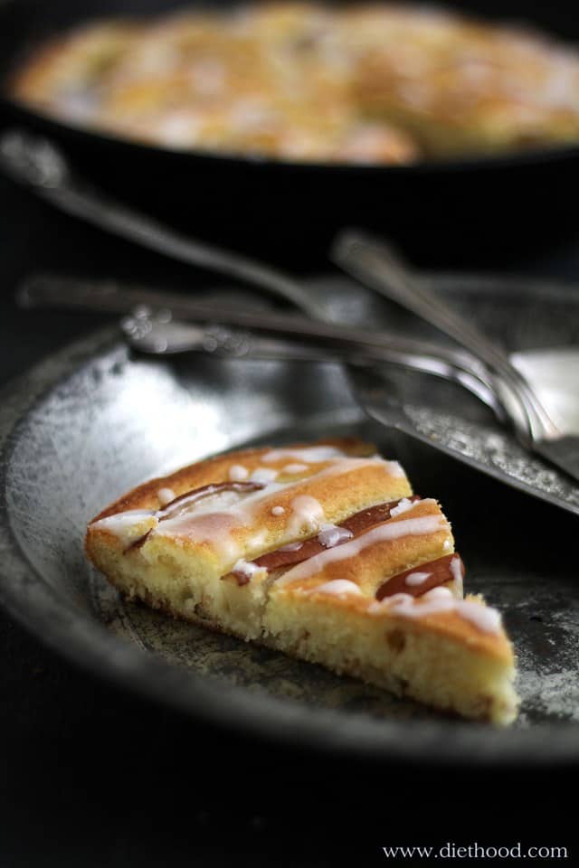 A slice of glazed pear cake on a tin plate with forks 