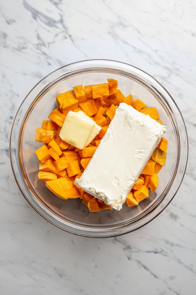 Cream cheese and butter added to a bowl with cubed sweet potatoes.