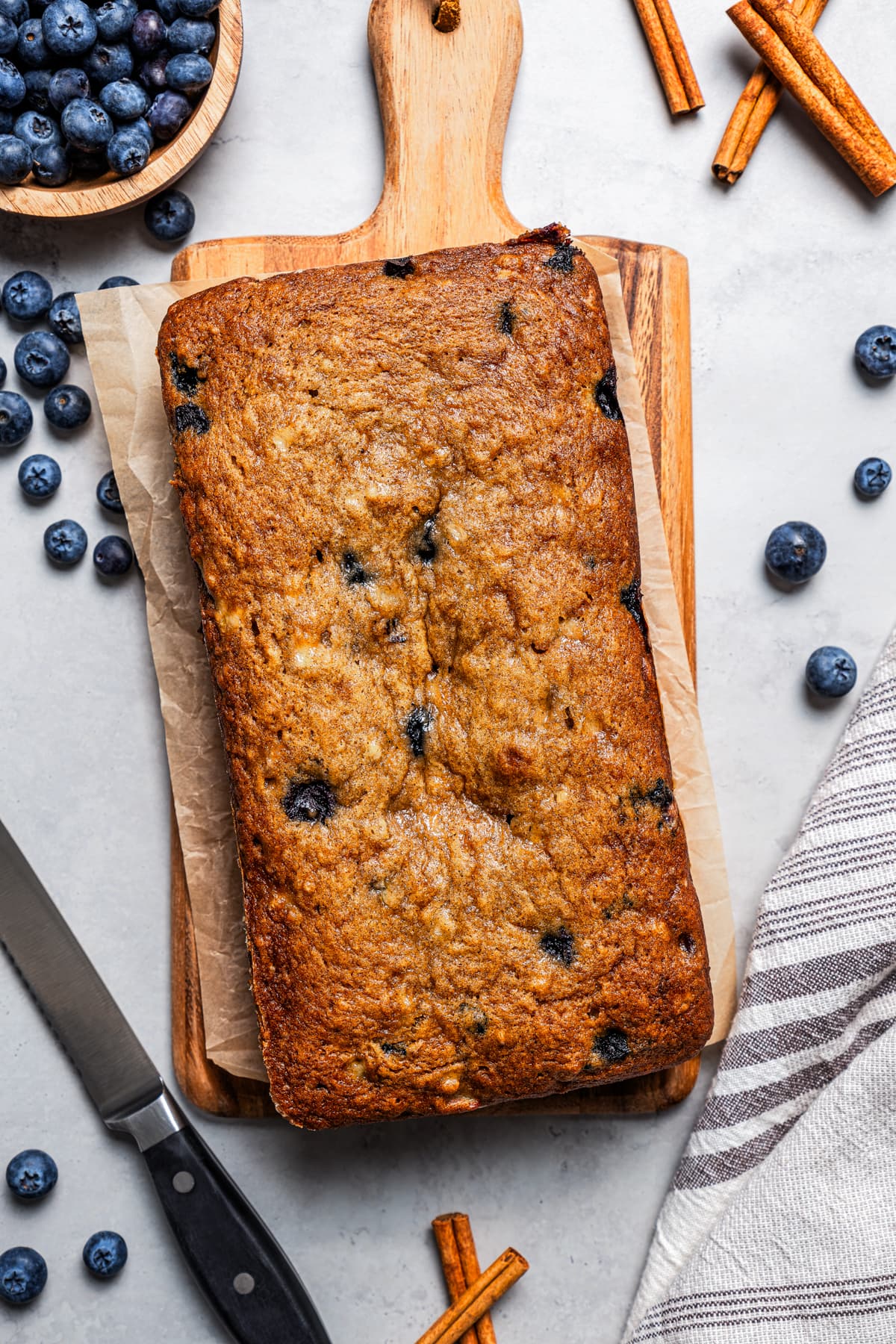 Overhead view of blueberry banana bread on a wooden board, surrounded by scattered blueberries.