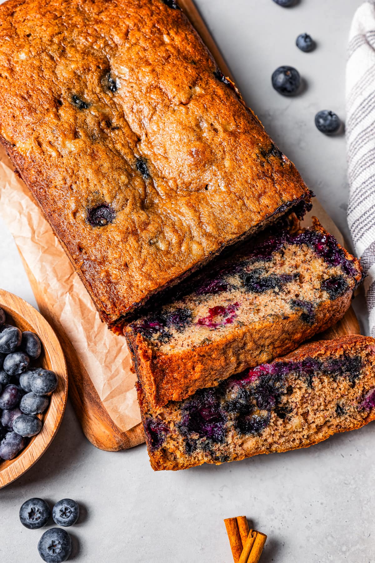 Overhead view of a loaf of blueberry banana bread cut into slices next to a bowl of blueberries.