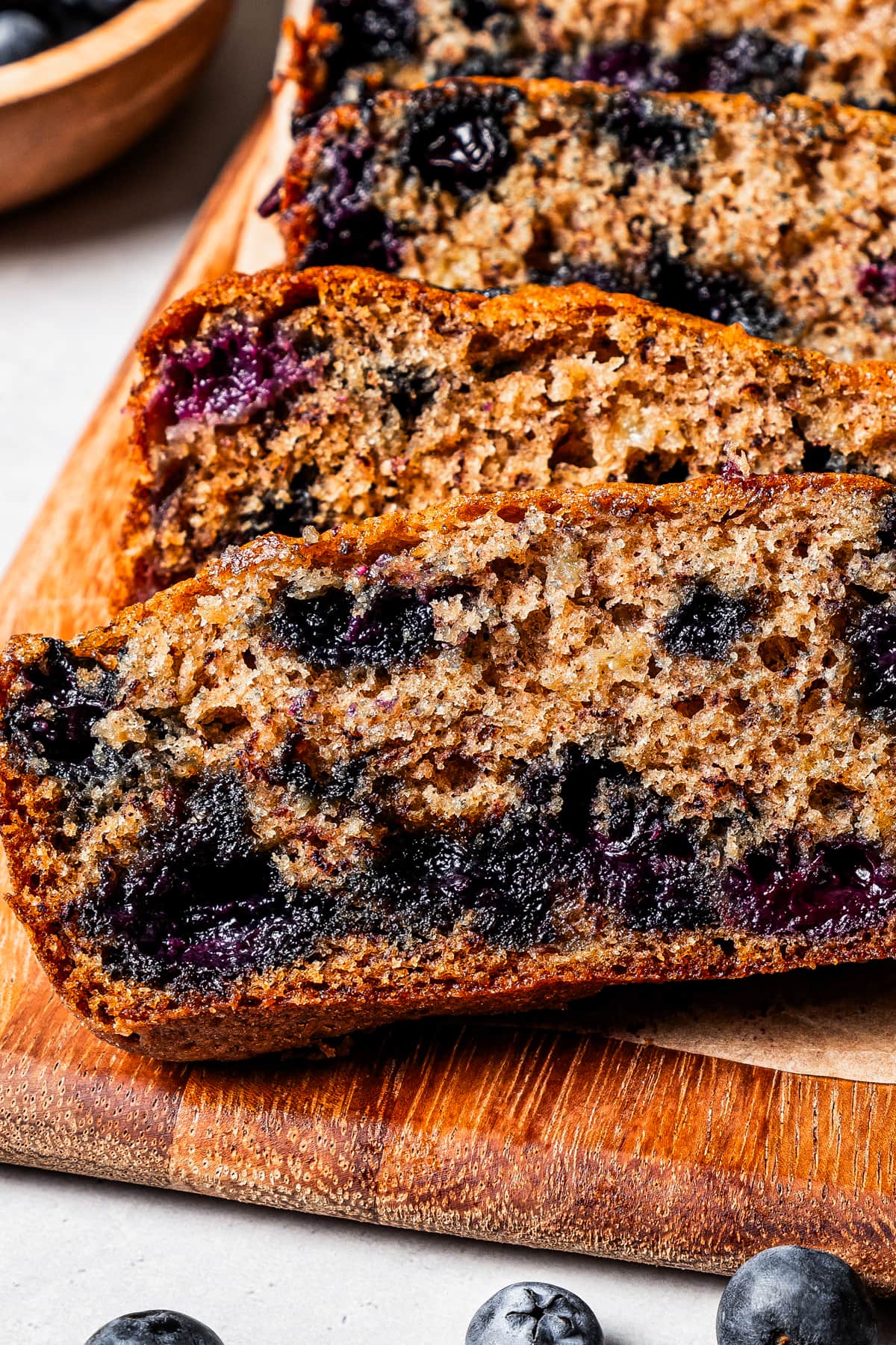 Close-up view of a loaf of blueberry banana bread cut into slices on a wooden platter.